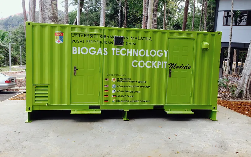 Grüner 20-Fuß-Container mit der Aufschrift „Universiti Kebangsaan Malaysia · Pusat Penyelidikan Tasik Chini · Biogas Technology Cockpit Module“ und der Liste der beteiligten Partner